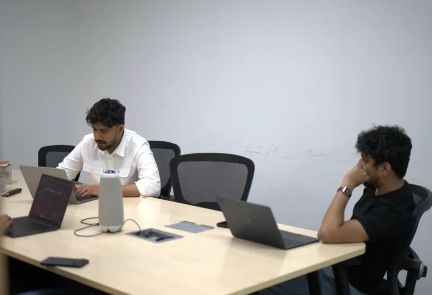 Two team members working at laptops on either side of a meeting table.