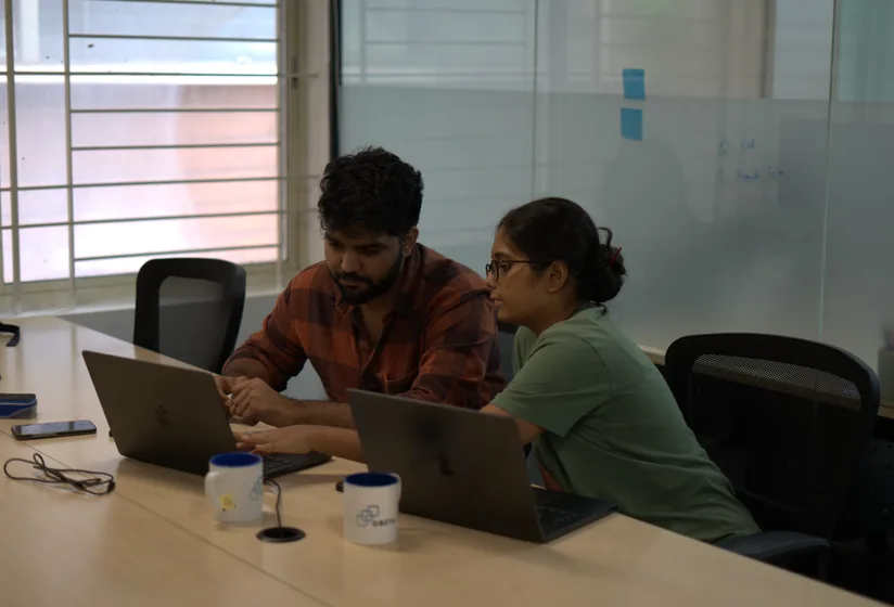 Two team members side by side at a desk, looking at the same laptop.